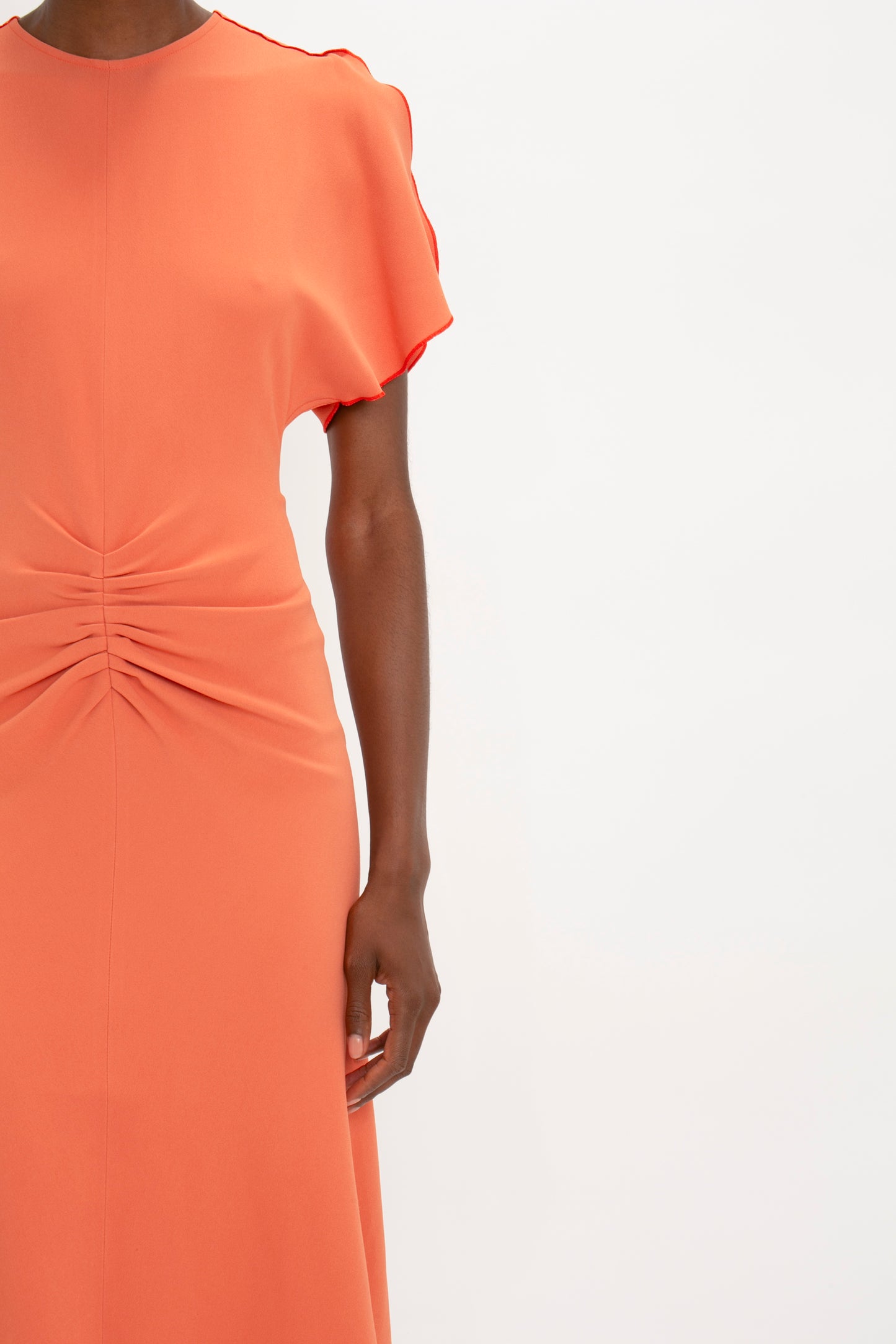 Close-up of a woman in a Victoria Beckham Gathered Waist Midi Dress In Papaya with ruffled sleeves, standing against a plain background.