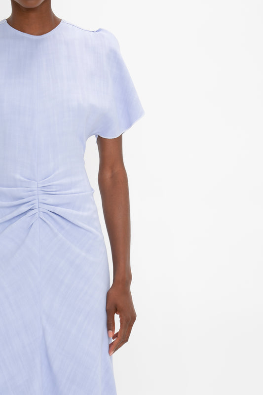 Partial view of a woman wearing a light blue Gathered Waist Midi Dress In Frost by Victoria Beckham, against a white background.