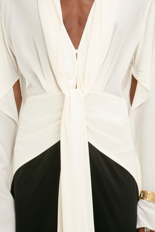 Close-up of a person wearing a Victoria Beckham Tie Detail Gown in Vanilla-Black, paired with a black skirt, against a neutral background.