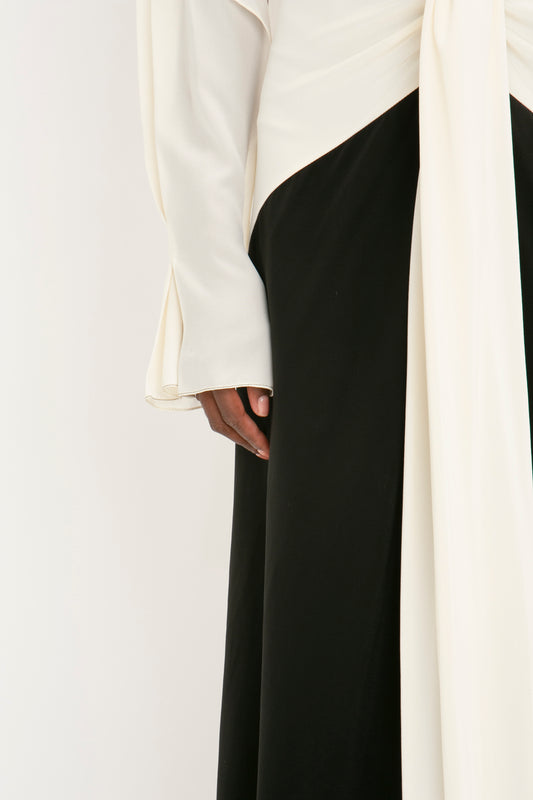A close-up photo of a person wearing a Victoria Beckham Tie Detail Gown In Vanilla-Black, with one hand tucked in the black skirt section.