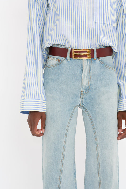 Midsection of a person wearing a blue striped shirt and Victoria Beckham's Bianca Jean In Light Blue Denim with a red belt.