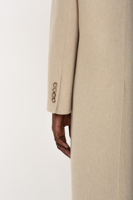 Close-up of a person in a Victoria Beckham Tailored Slim Coat In Bone with decorative buttons on the sleeve, hand visible from the coat's side slit.