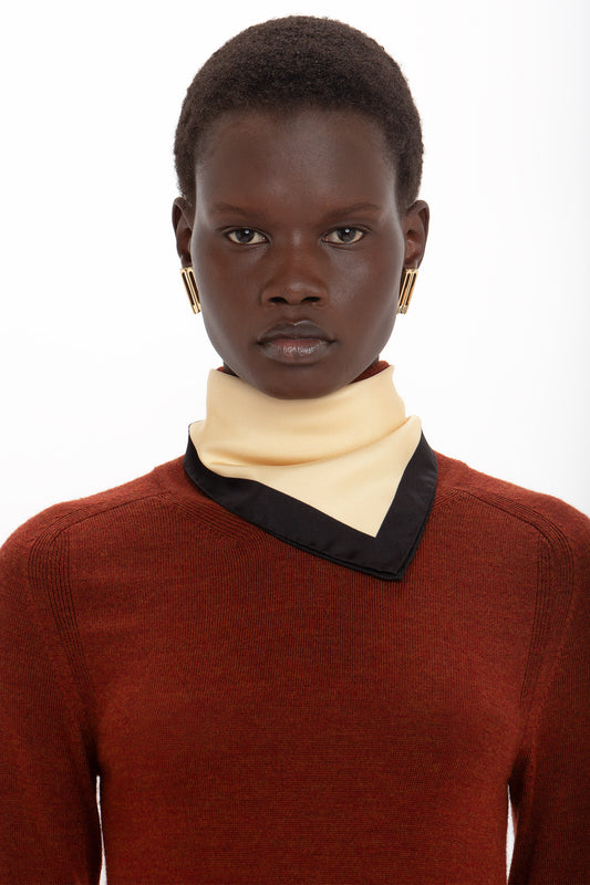 A person with short black hair wearing large hoop earrings, a red sweater made from Victoria Beckham printed silk twill, and a yellow collar with black trim, against a white background.