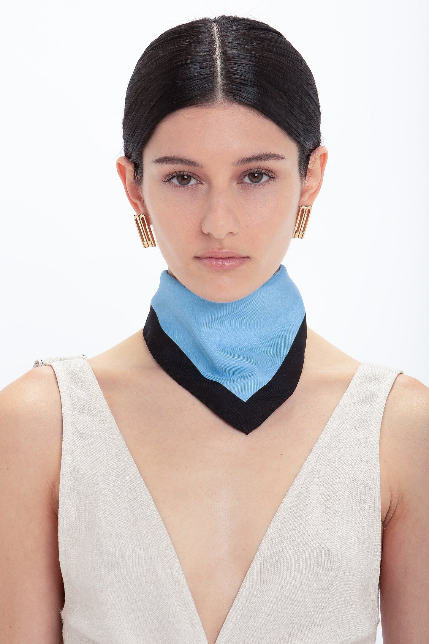 Woman with center-parted dark hair, wearing large hoop earrings, a beige dress, and a Colour Block Foulard In Marina printed silk twill with black border from Victoria Beckham.