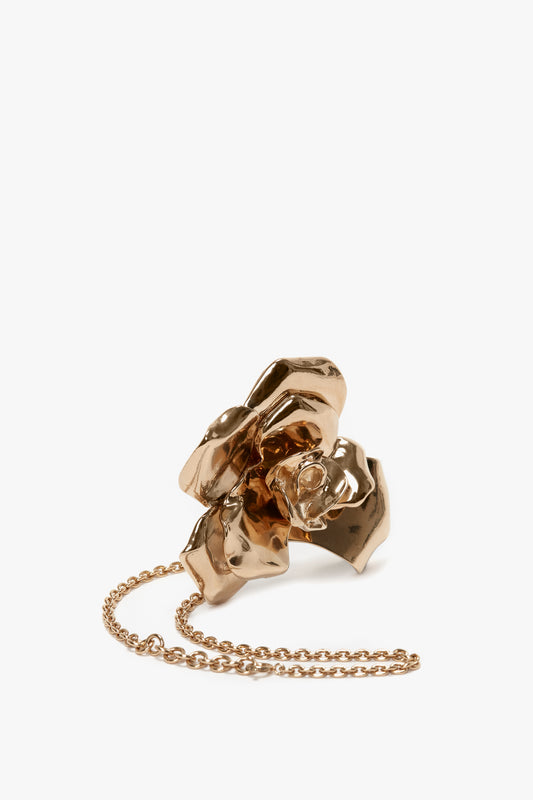 A Victoria Beckham gold brushed brass clutch bag designed to resemble a crumpled piece of paper, attached to a thin gold chain, isolated on a white background.