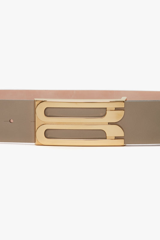 A close-up of a Exclusive Jumbo Frame Belt In Beige Leather by Victoria Beckham with a unique gold buckle shaped in a stylized, modern design, isolated on a white background.