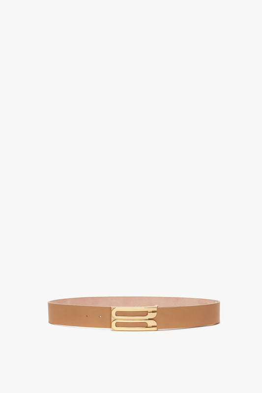 A Jumbo Frame Belt In Camel Leather by Victoria Beckham with a unique gold buckle, displayed against a plain white background.