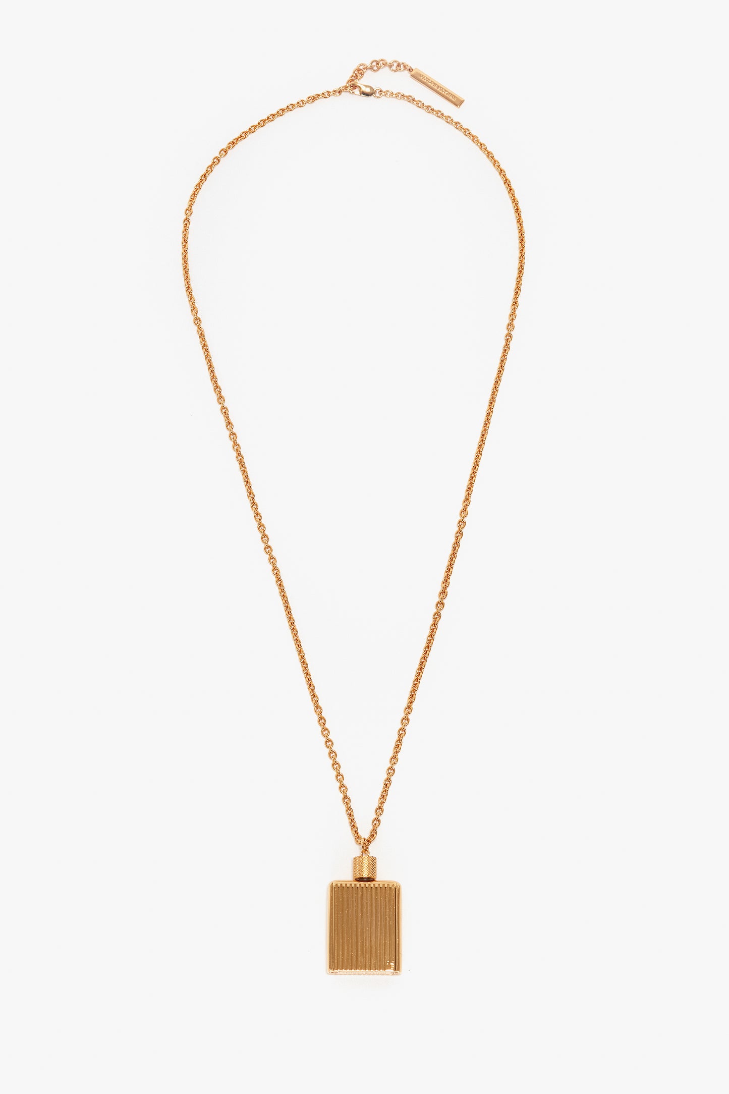 A gold necklace with a rectangular, gold brushed brass pendant featuring vertical grooves, reminiscent of the Victoria Beckham Exclusive Perfume Bottle Necklace In Brushed Gold.