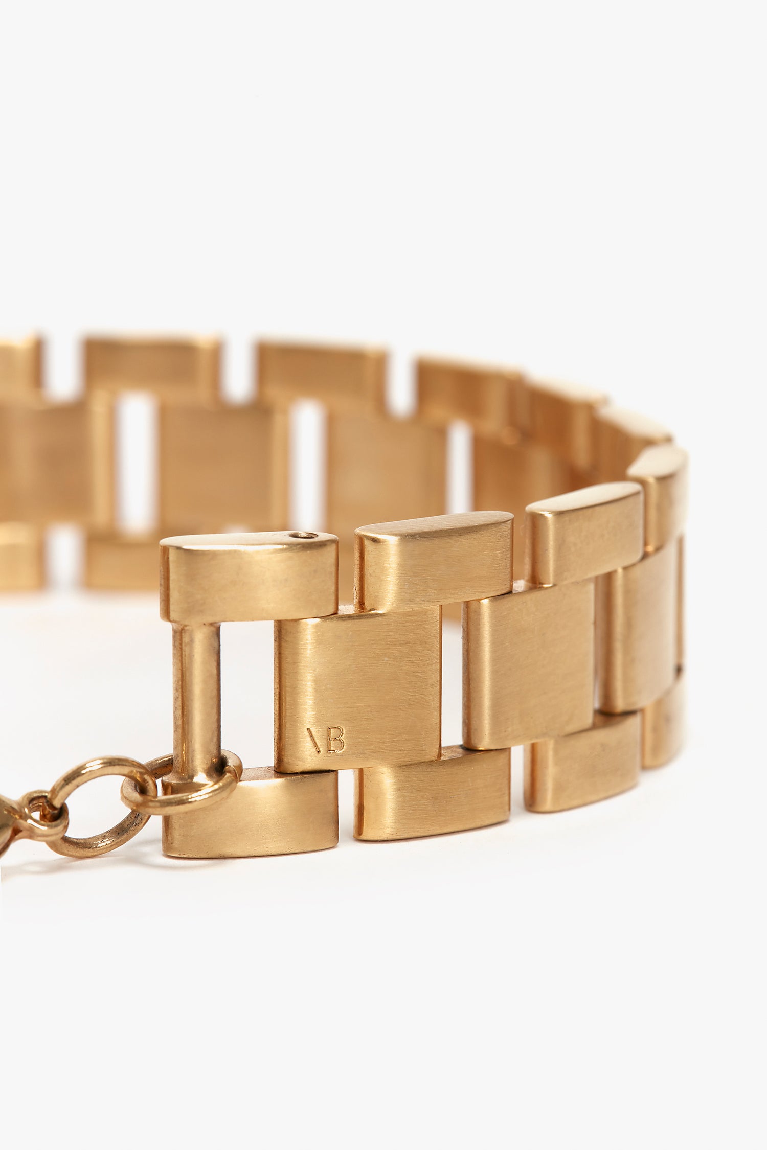 Close-up of an Exclusive Chain Wrap Necklace In Brushed Gold with rectangular segments and a chain clasp. The initials "VB" are engraved on one of the links, showcasing the Victoria Beckham logo.
