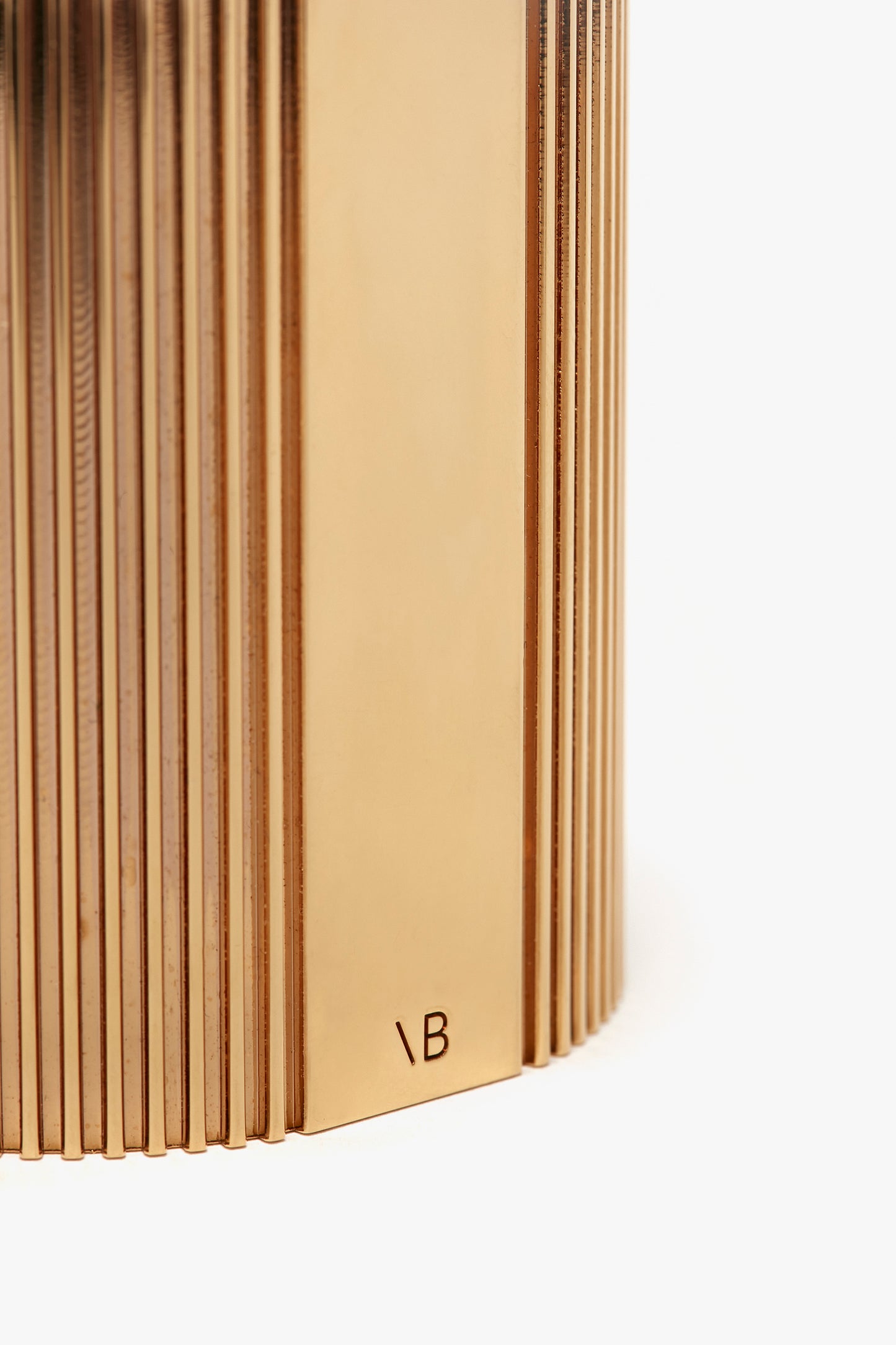 Close-up image of the side view of an open book with beige pages, focusing on the textured edges and a visible 'nb' imprint on the Victoria Beckham Exclusive Perfume Cuff In Gold back cover.