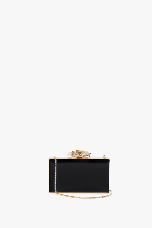 Elegant Victoria Beckham black clutch with a golden floral clasp and a detachable shoulder strap, isolated against a white background.