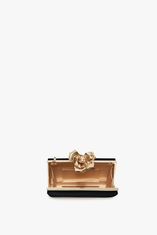 A small, elegant Victoria Beckham black Frame Flower Minaudiere clutch purse with a prominent gold floral clasp and a detachable shoulder strap, displayed against a white background.