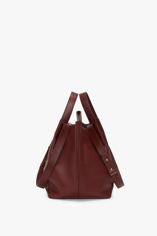 A Victoria Beckham Medium Tote In Burgundy Leather stands upright against a white background, displaying side pockets and a partially visible interior.