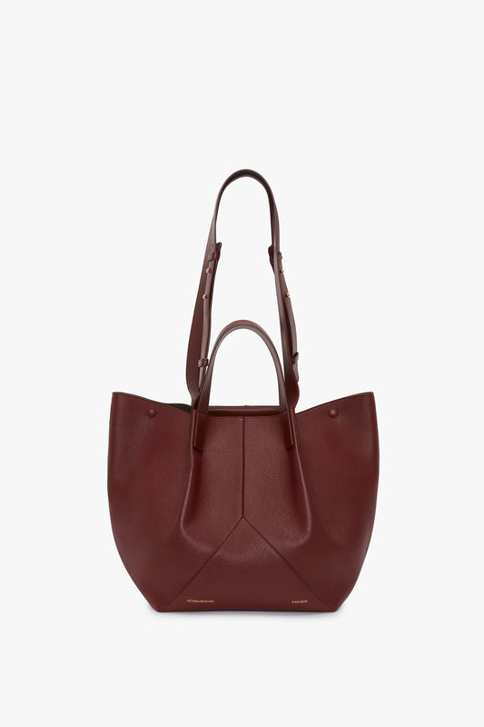 The Victoria Beckham Medium Tote In Burgundy Leather with a structured design and dual handles, displayed against a neutral background.