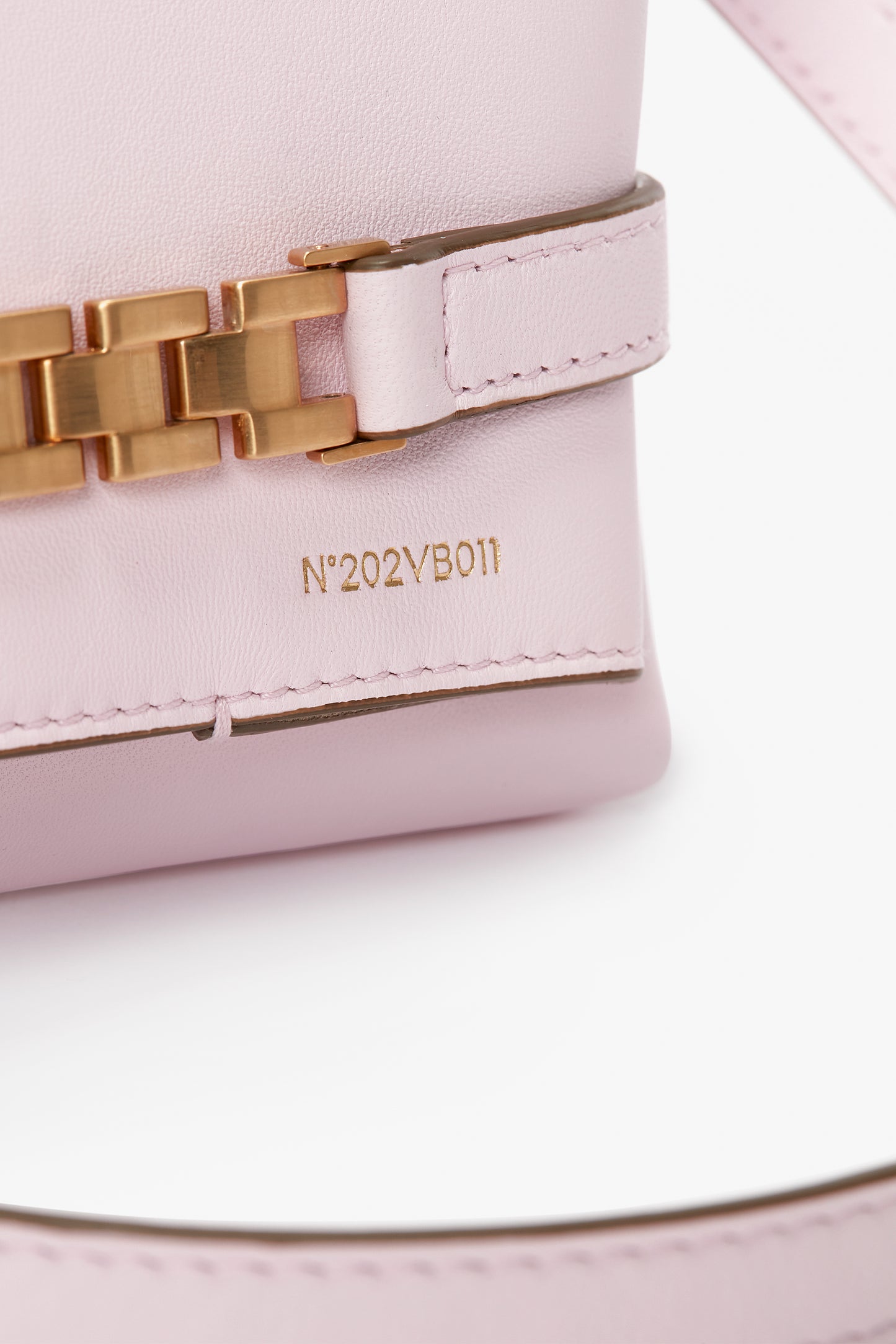 Close-up of a bubblegum pink leather Exclusive Mini Chain Pouch Bag With Long Strap In Bubblegum Pink Leather by Victoria Beckham with a gold chain detail and the embossed text "N°202VB011" on its surface.