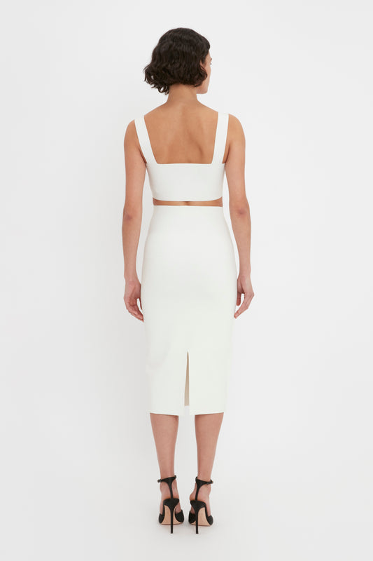 A woman in a Victoria Beckham VB Body Strap Bandeau Top In White and black heels viewed from behind against a plain background.