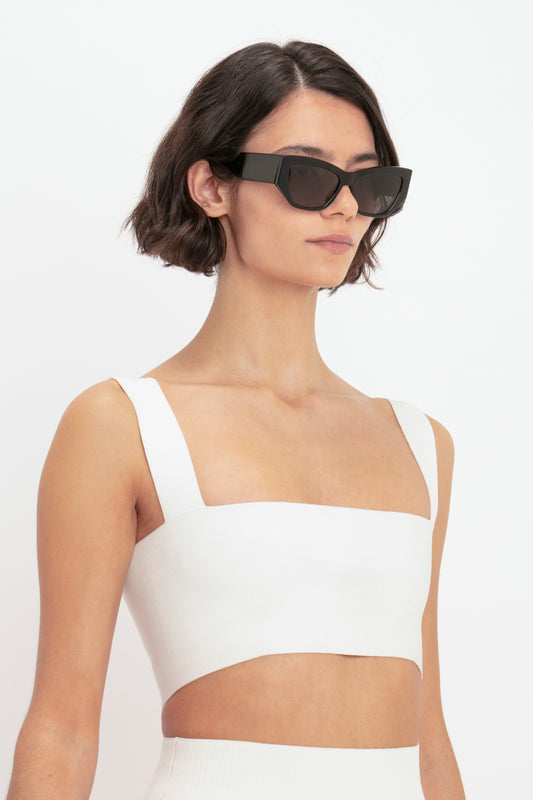 A woman with short brown hair wearing oversized black sunglasses and a Victoria Beckham Body Strap Bandeau Top in White against a plain background.