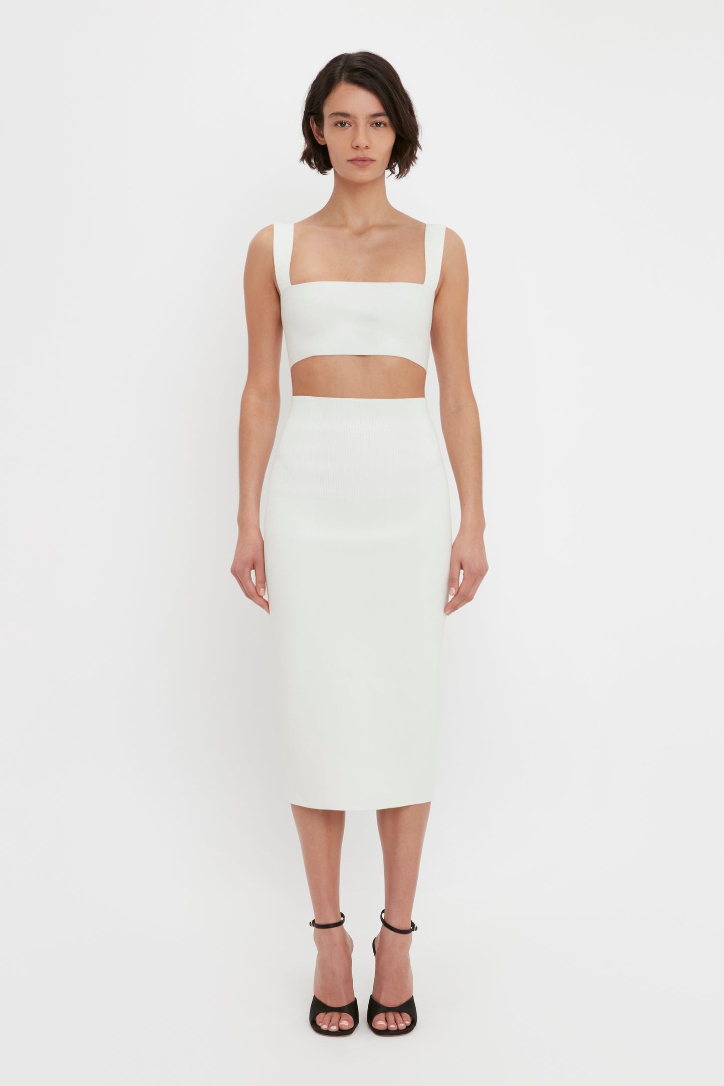 A woman wearing a white strap VB Body Strap Bandeau Top in White and matching VB Body Fitted Midi Skirt stands facing forward against a plain white background.