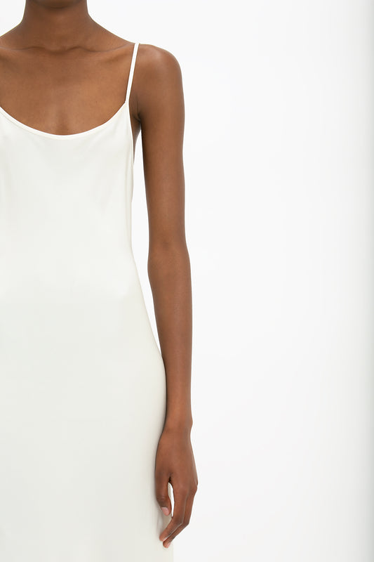 Close-up of a woman wearing a Victoria Beckham floor-length cami dress in ivory, focusing on her shoulder and arm against a plain background.