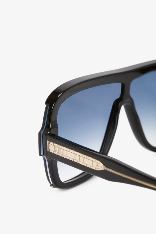 Close-up of Victoria Beckham Layered Mask Sunglasses In Black Gradient with a textured metallic detail on the arms, against a white background.