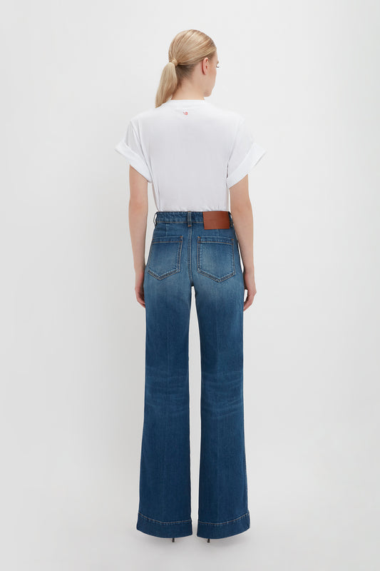 Woman standing with her back to the camera, wearing a white oversized Victoria Beckham T-shirt and blue Alina jeans in dark vintage wash, paired with a brown belt.