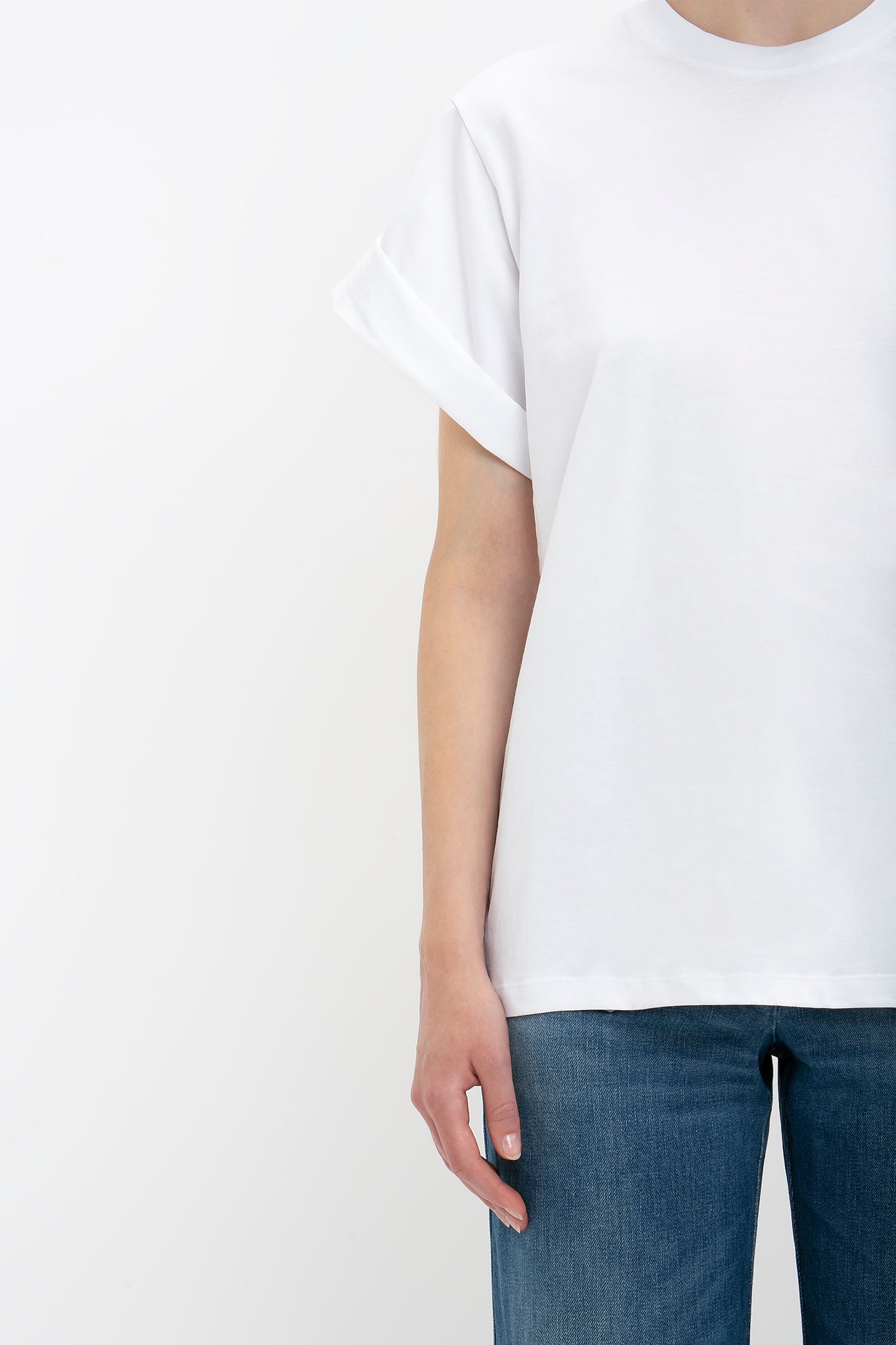 A person wearing an oversized Victoria Beckham white T-shirt and blue jeans, shown from the waist down to mid-thigh, with a focus on the T-shirt.