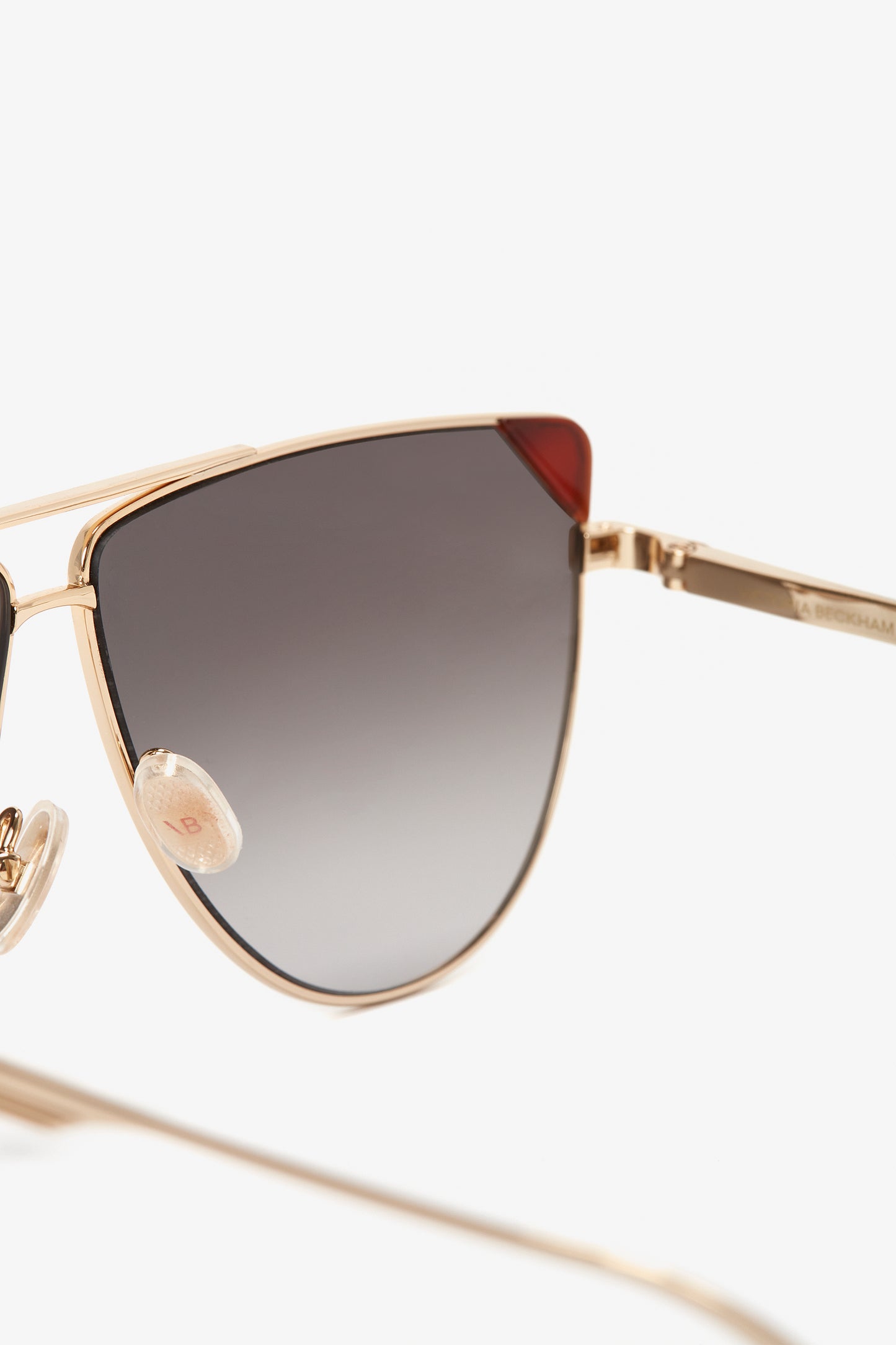 Close-up of stylish Victoria Beckham V-Line Aviator In Gold Blonde Havana sunglasses with caramel gradient lenses, gold metal frames, and red corner accents.