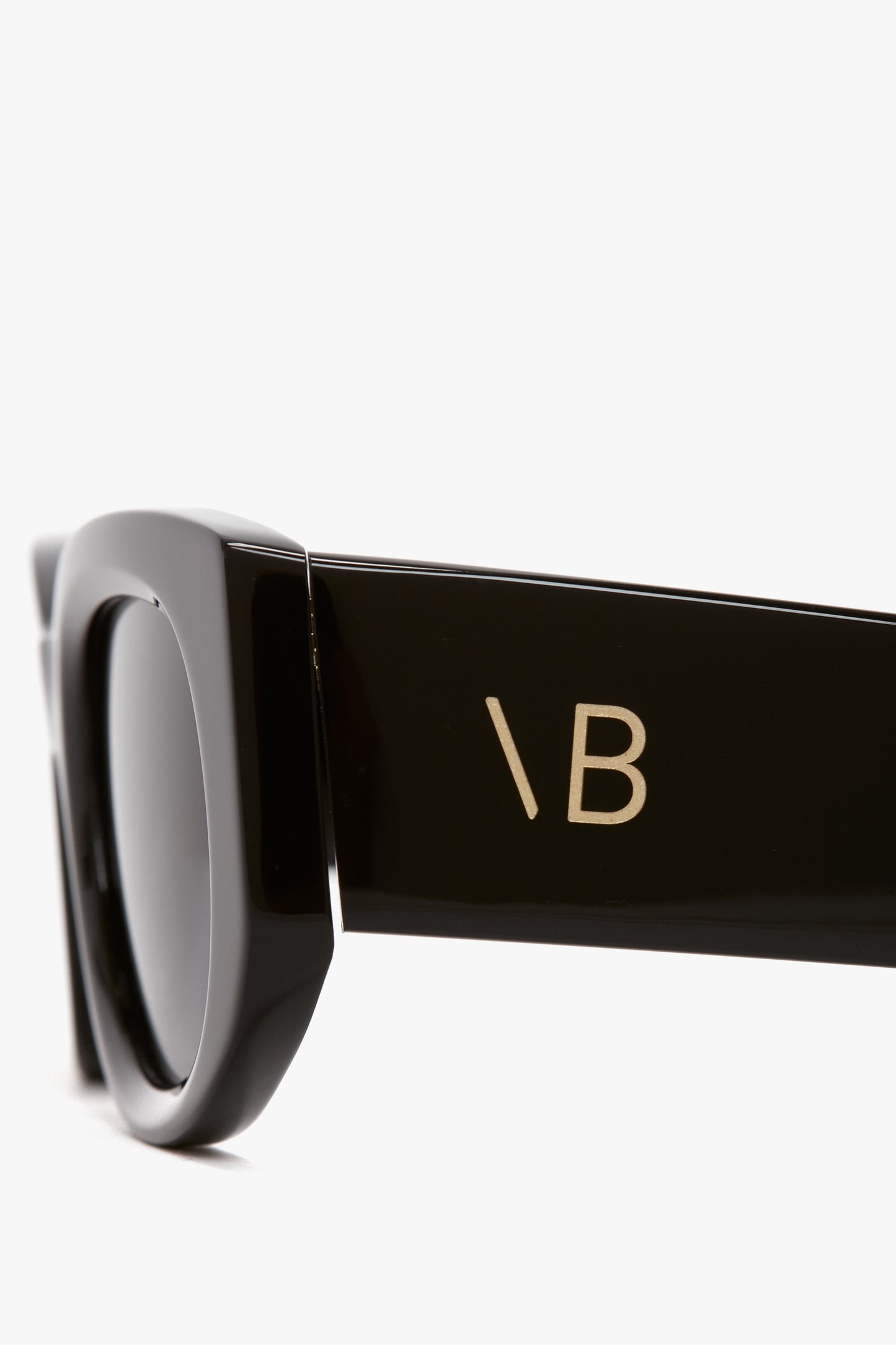 Close-up view of black Victoria Beckham Monogram Detail Sunglasses In Black featuring the initials "VB" in white on the side of the arm.