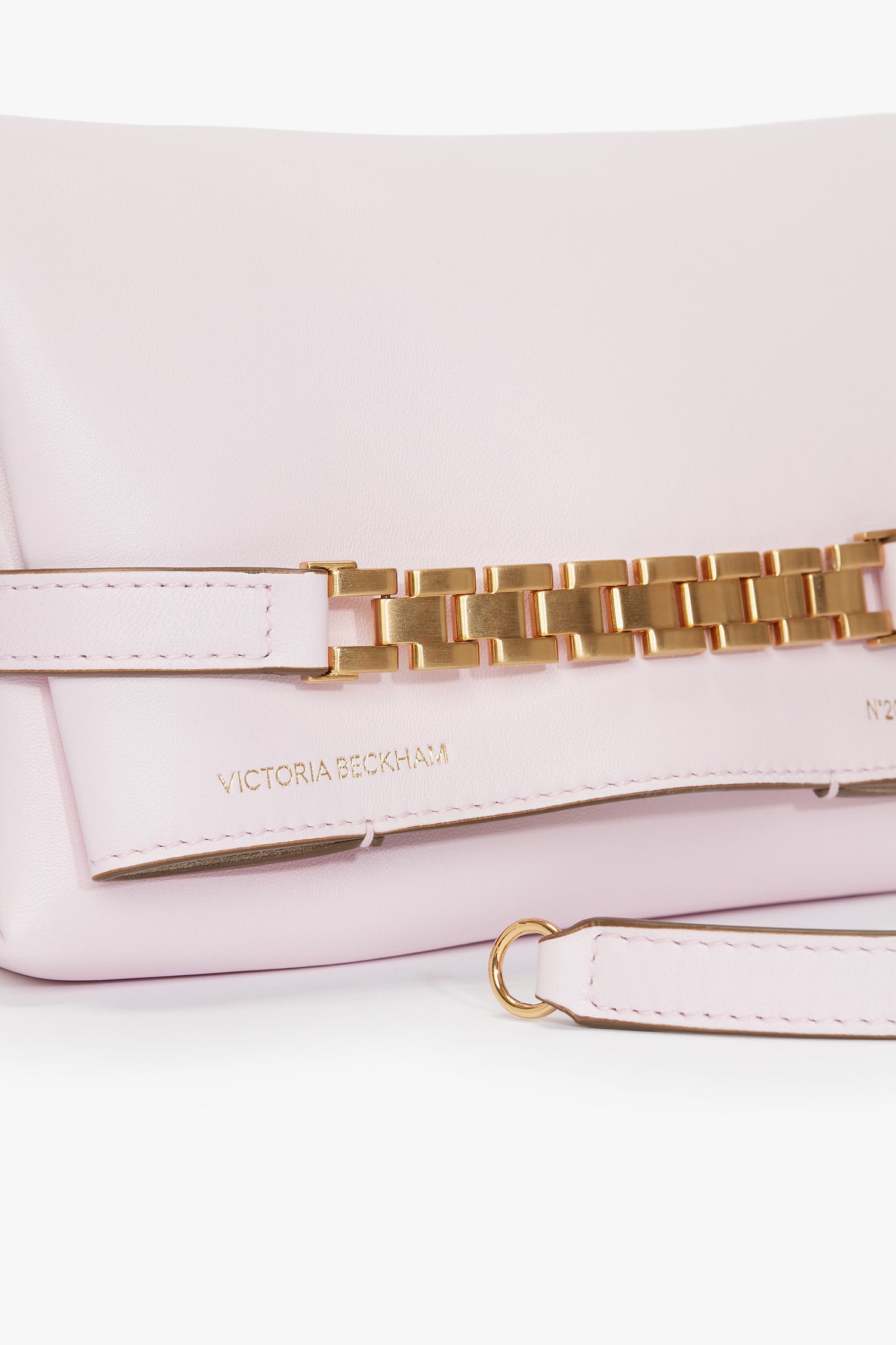 A bubblegum pink handbag with a gold chain detail, bearing the brand name "Victoria Beckham" embossed on the front. This lovely Exclusive Mini Chain Pouch Bag With Long Strap In Bubblegum Pink Leather also features a detachable strap for versatile carrying options.