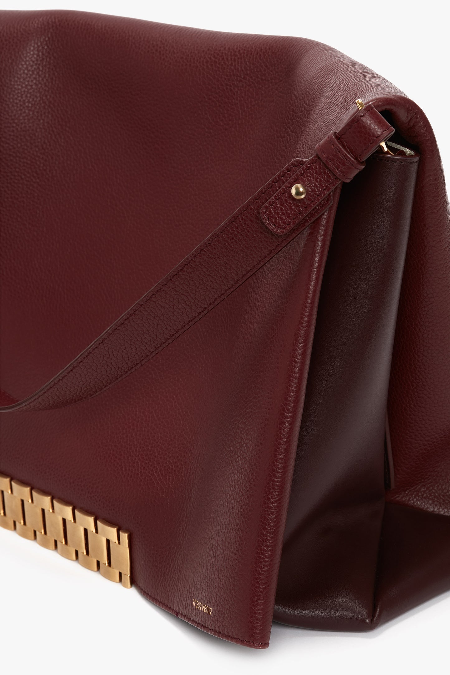 A Jumbo Chain Pouch Bag In Bordeaux Leather with a shoulder strap and a gold accent along the bottom edge is shown on a white background, featuring a detachable strap for versatility. This product is from Victoria Beckham.
