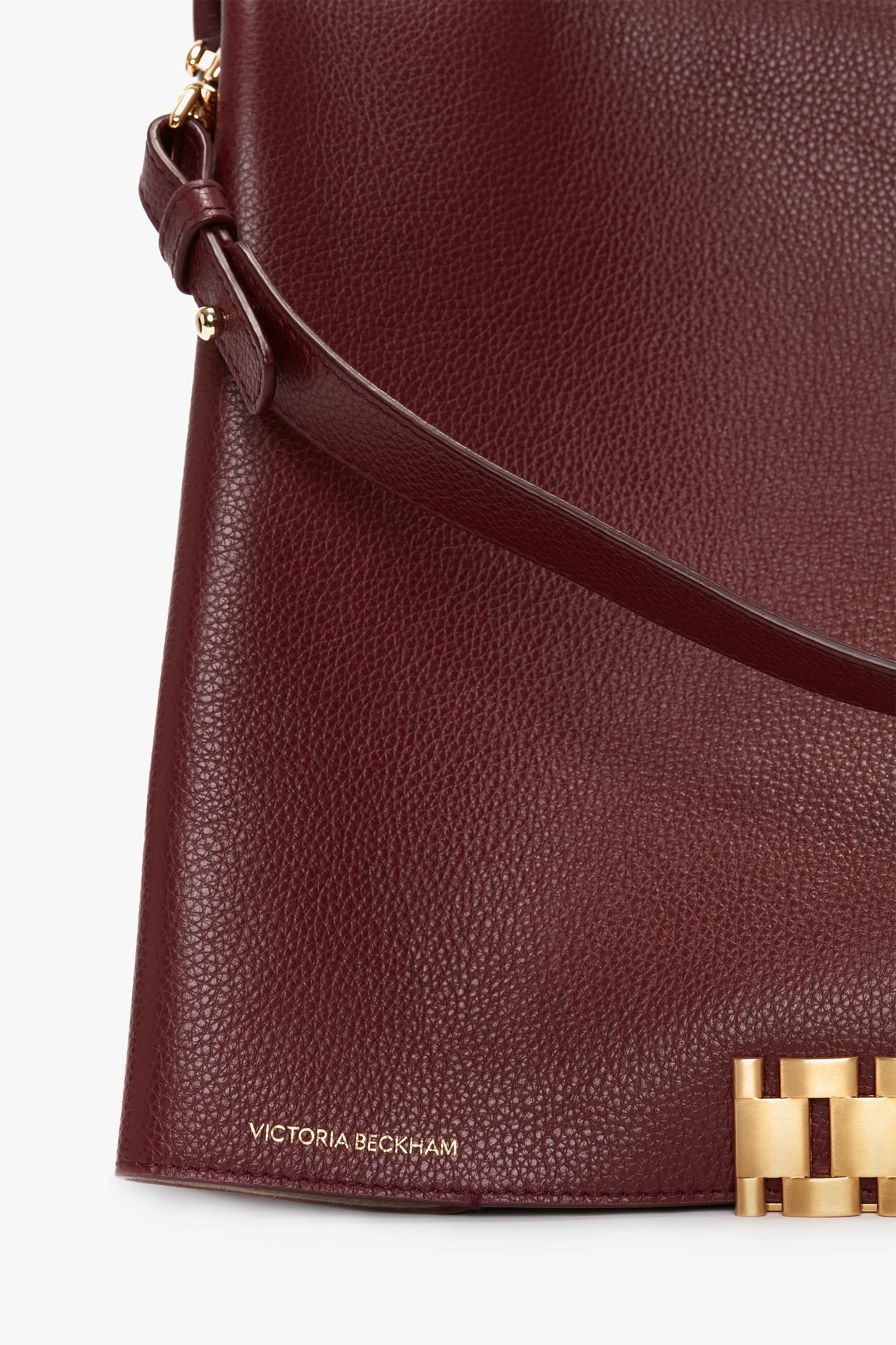 Close-up of a maroon grained leather Jumbo Chain Pouch Bag in Bordeaux Leather with a gold clasp detail and "Victoria Beckham" embossed in small gold letters at the bottom left corner, featuring a detachable strap for versatile wear.