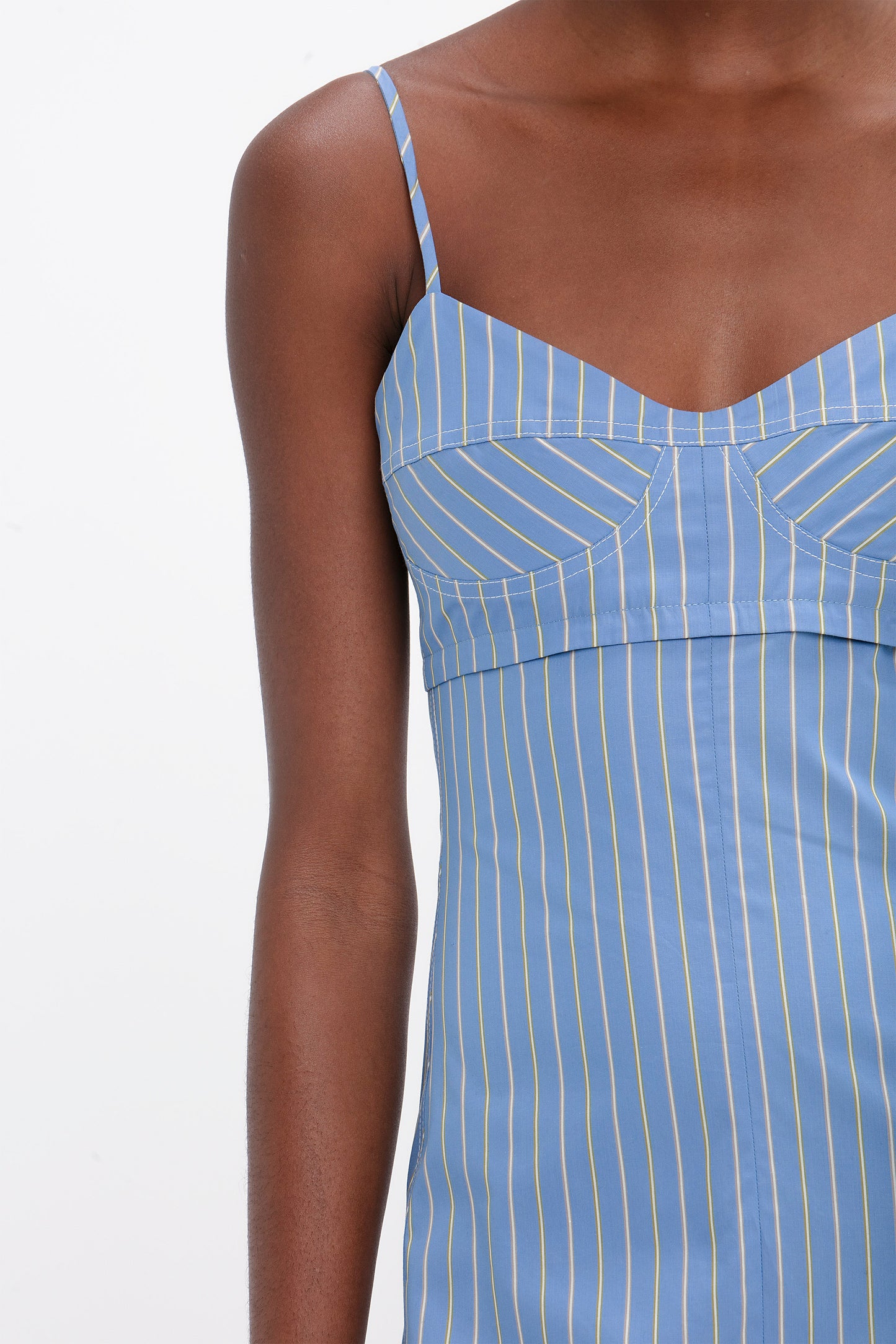 Close-up of a person wearing the Cami Fit And Flare Midi In Steel Blue by Victoria Beckham with thin yellow vertical stripes, paired perfectly with flat lace up mules.
