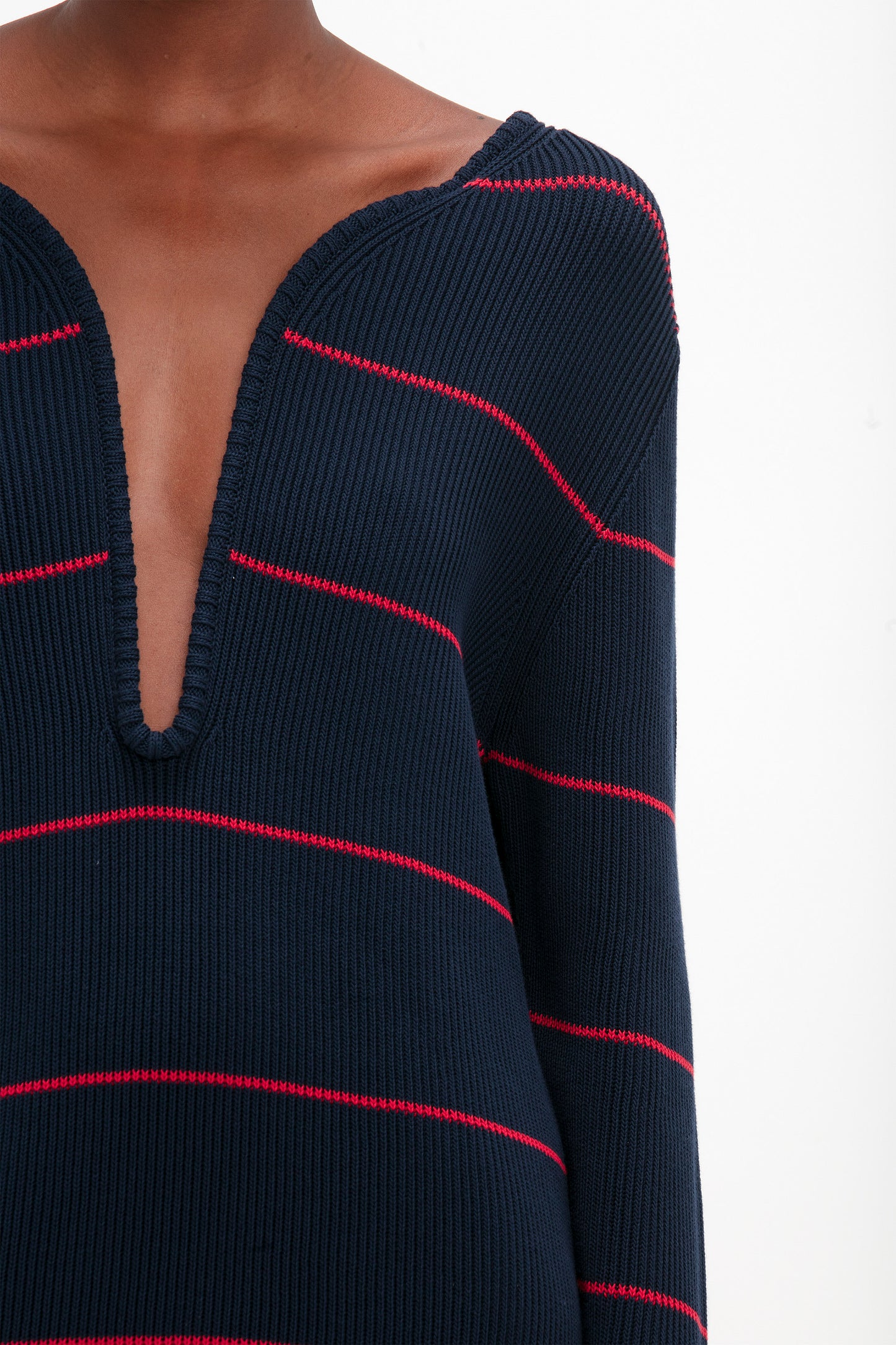 Close-up of a person wearing a Victoria Beckham Frame Detail Jumper Dress In Navy-Red, reminiscent of an SS24 runway look. The mid-weight knit garment stands out against the plain white background.
