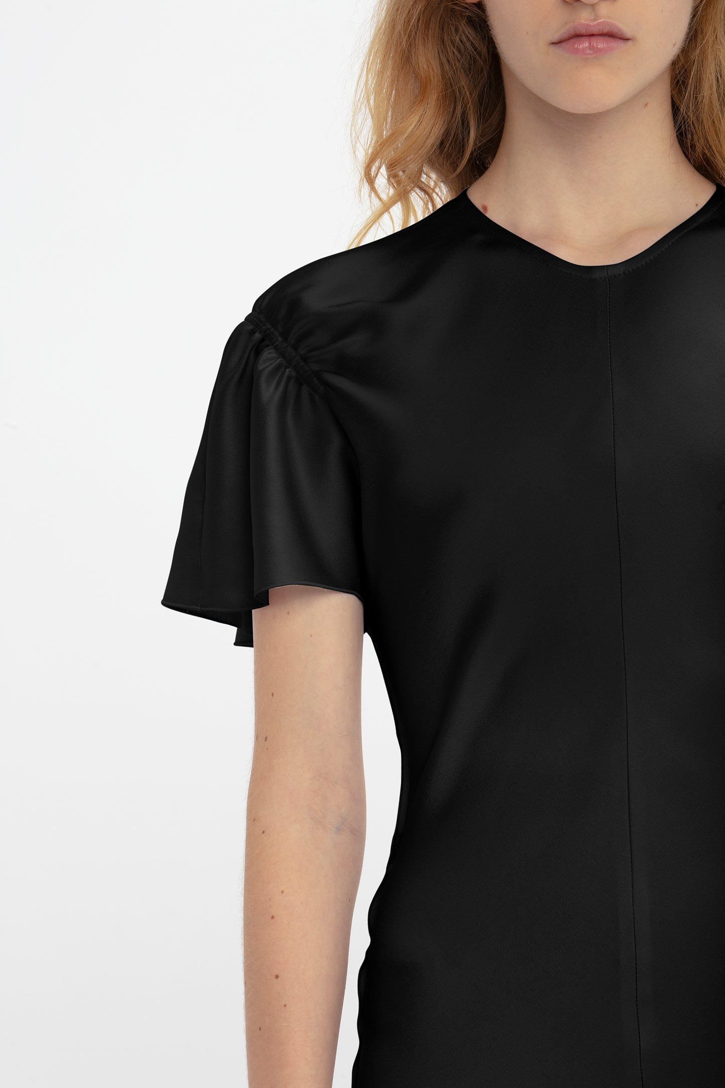 A person is shown from the shoulders up, wearing a Gathered Sleeve Midi Dress In Black by Victoria Beckham. The individual has light skin and long, light brown hair, with a neutral expression on their face.