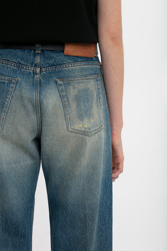 Close-up of a person wearing light blue Victoria Beckham relaxed straight leg jeans in antique indigo wash showing the back pocket and belt detail against a white background.
