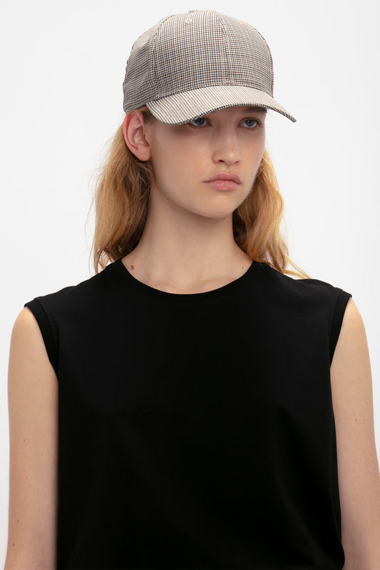 Young woman wearing a black sleeveless top and a gray wool Victoria Beckham Logo Cap In Dogtooth Check, posing against a white background.