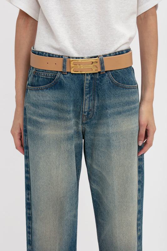 Close-up view of a person wearing blue jeans and a white t-shirt, accessorized with a Victoria Beckham Jumbo Frame Belt In Camel Leather featuring gold hardware.