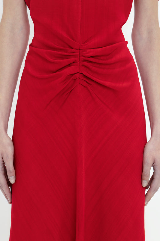 Close-up of a woman in a Victoria Beckham Exclusive Gathered V-Neck Midi Dress In Carmine with hands resting on her hips, detail of gathered fabric at the waist.