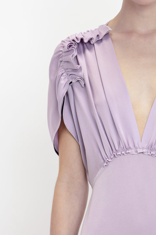 Close-up of a person wearing an elegant Victoria Beckham brand V-Neck Ruffle Midi Dress In Petunia with a deep V-neck and ruffled shoulder detail.