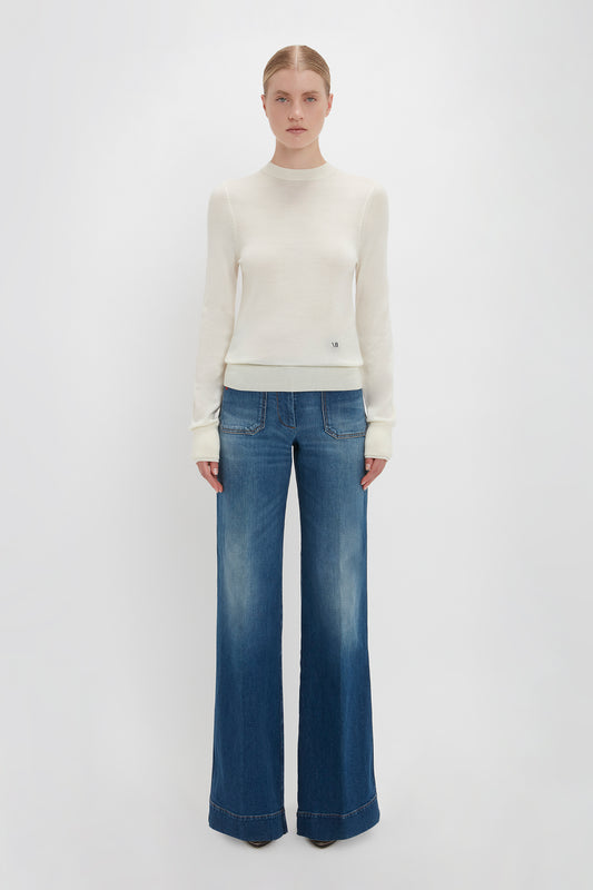 Woman in a Victoria Beckham Merino Crew Jumper In Ivory and blue flared jeans standing against a plain white background.