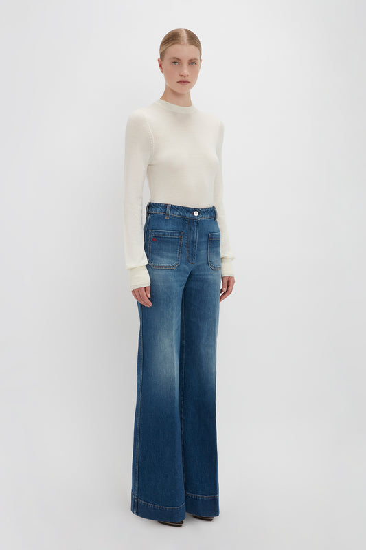 Woman in a Victoria Beckham Merino Crew Jumper In Ivory and blue wide-leg jeans standing against a plain white background.