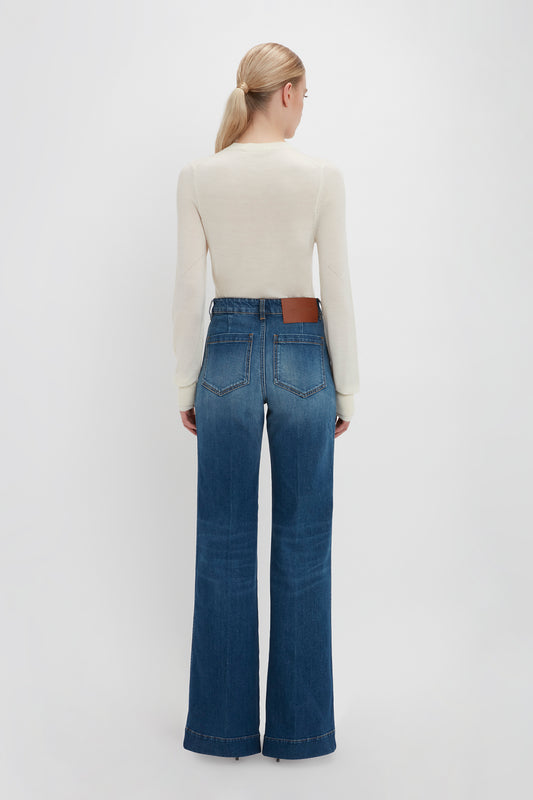 Woman standing with her back facing the camera, wearing blue jeans and a Victoria Beckham Merino Crew Jumper In Ivory, against a plain white background.