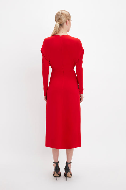 A woman in a red Victoria Beckham Dolman Midi Dress and black Pointy Toe Stiletto heels stands with her back to the camera against a white background.