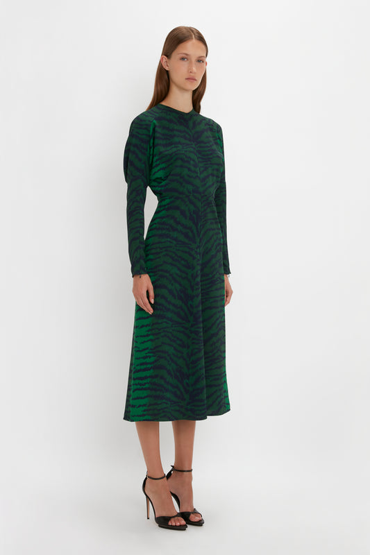 A woman in a Victoria Beckham green-navy tiger print Dolman midi dress and pointy toe stiletto heels standing against a white background.
