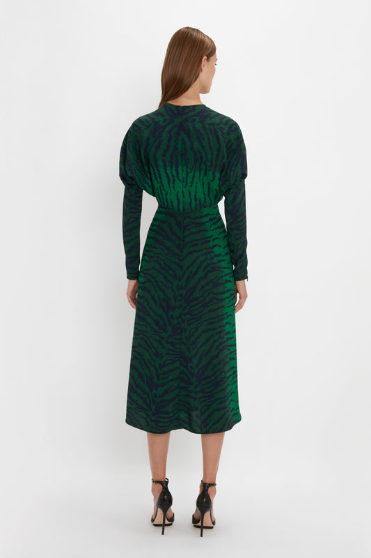 Woman standing with her back to the camera, wearing a Victoria Beckham Dolman Midi Dress In Green-Navy Tiger Print and black pointy toe stilettos, against a white background.