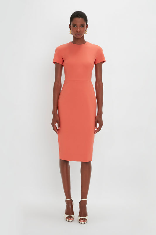 A black woman wearing an orange Victoria Beckham Fitted T-Shirt Dress In Papaya with short sleeves and strappy sandals, standing against a plain white background.