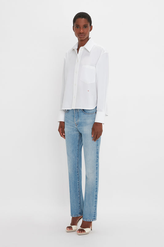 A black woman in a Victoria Beckham classic white shirt and blue jeans, standing against a plain white background. She is wearing silver heels.