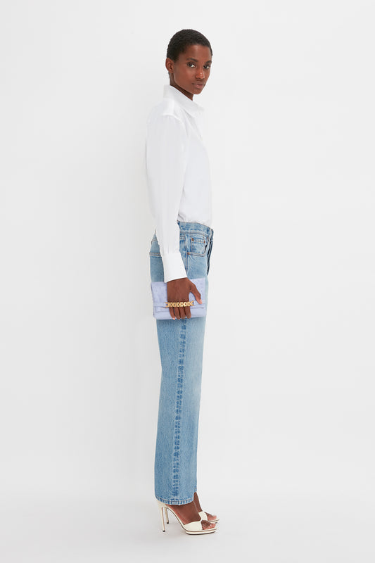 Woman in classic Victoria Beckham cropped long sleeve shirt in white and blue jeans standing sideways, looking over her shoulder, with a white background.