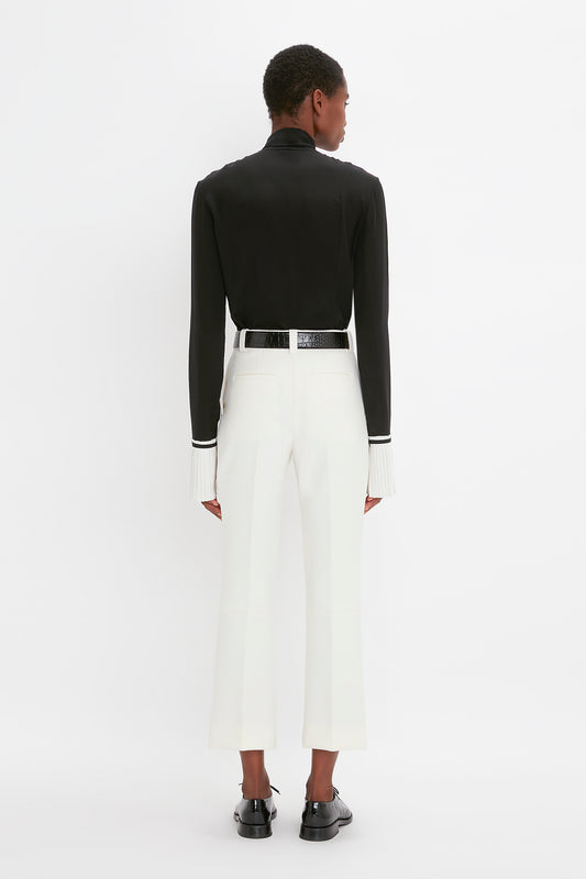 Woman in a chic black and white outfit featuring a black jacket and Victoria Beckham cropped kick trousers in ivory, viewed from behind. She is standing against a plain background.