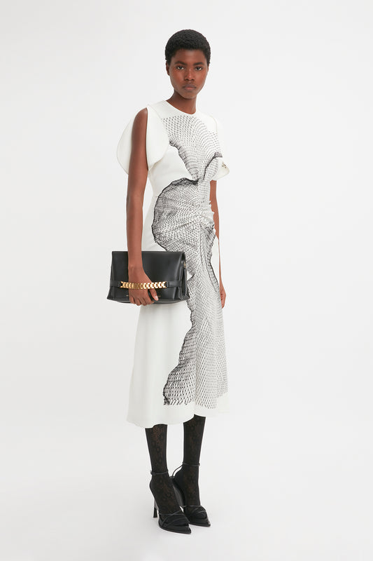 A black woman models a Victoria Beckham gathered waist midi dress in white-black contorted net print, paired with black boots and holding a clutch.